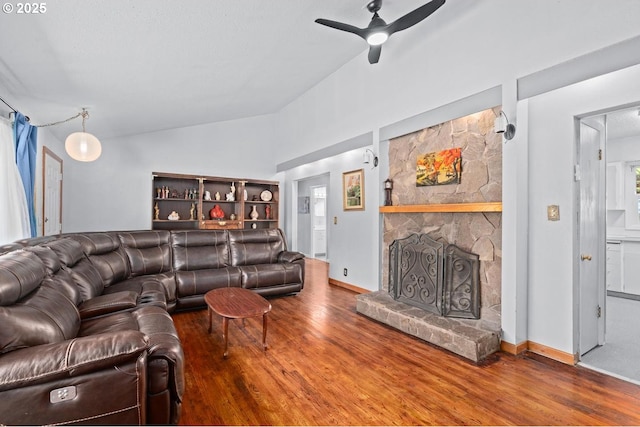 living area with a ceiling fan, baseboards, vaulted ceiling, a fireplace, and wood finished floors