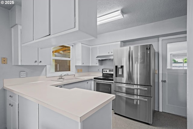 kitchen with a peninsula, a sink, under cabinet range hood, light countertops, and appliances with stainless steel finishes