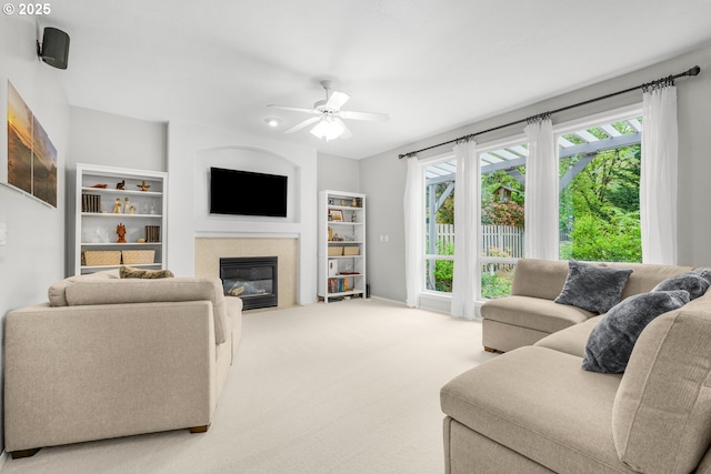 living area featuring carpet flooring, a ceiling fan, a fireplace with flush hearth, and a healthy amount of sunlight