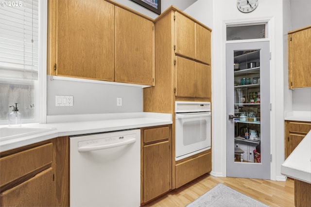kitchen featuring light wood-style floors, light countertops, white appliances, and a sink