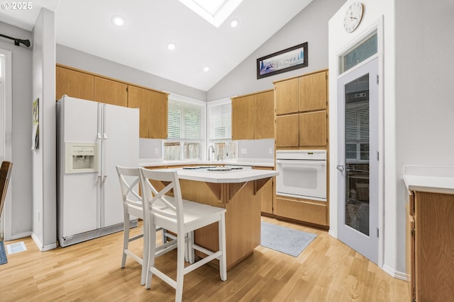 kitchen with white appliances, light wood-style floors, a breakfast bar area, a center island, and light countertops