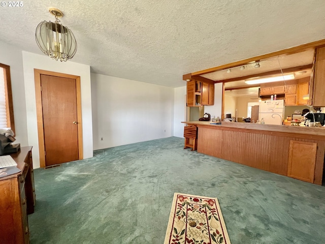 kitchen with carpet floors, brown cabinets, freestanding refrigerator, an inviting chandelier, and a textured ceiling