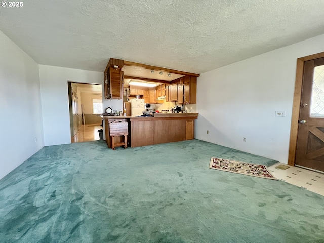 kitchen with brown cabinetry, a peninsula, freestanding refrigerator, a textured ceiling, and light colored carpet