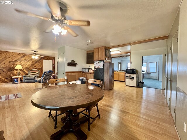 dining area with ceiling fan, wooden walls, light wood-style flooring, and a textured ceiling