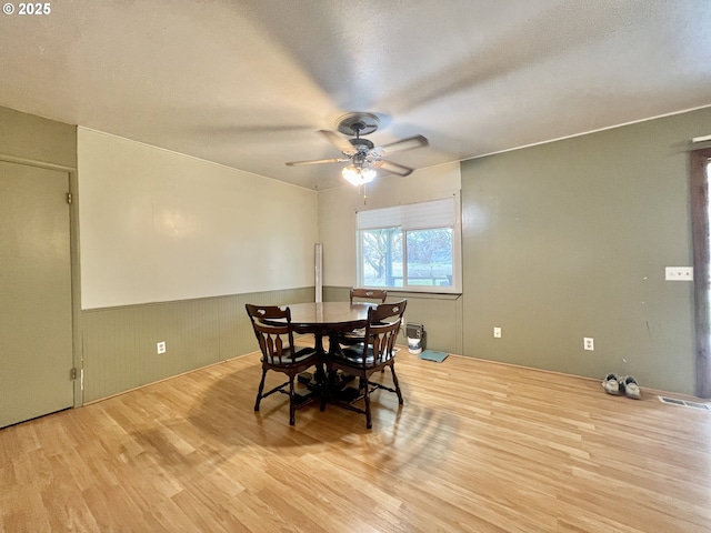 dining space with visible vents, a wainscoted wall, wood finished floors, a textured ceiling, and a ceiling fan