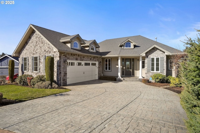 view of front of home with a garage, stone siding, decorative driveway, and roof with shingles