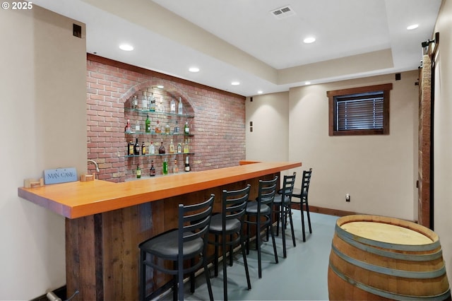 bar featuring finished concrete flooring, recessed lighting, visible vents, brick wall, and baseboards