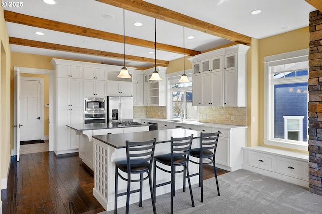 kitchen featuring stainless steel appliances, a breakfast bar, a kitchen island, beam ceiling, and decorative backsplash