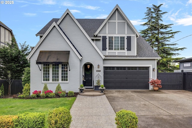 tudor home with concrete driveway, a shingled roof, an attached garage, and fence