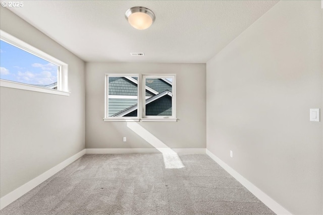 spare room featuring carpet, visible vents, a textured ceiling, and baseboards