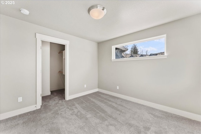 unfurnished bedroom with carpet, baseboards, a walk in closet, and a textured ceiling