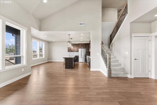 unfurnished living room with baseboards, visible vents, stairway, wood finished floors, and high vaulted ceiling