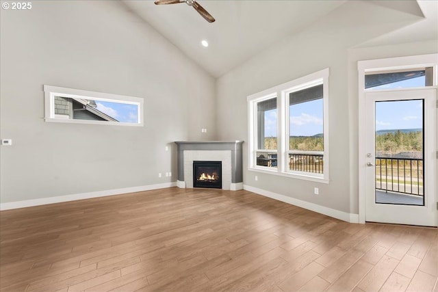 unfurnished living room with light wood finished floors, a brick fireplace, ceiling fan, high vaulted ceiling, and baseboards