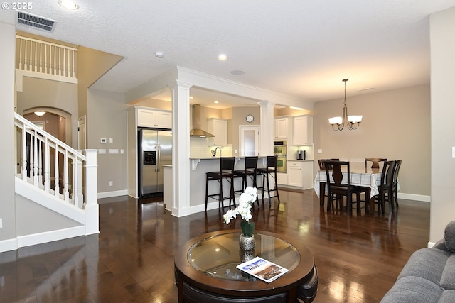 living room with an inviting chandelier, dark hardwood / wood-style flooring, and decorative columns