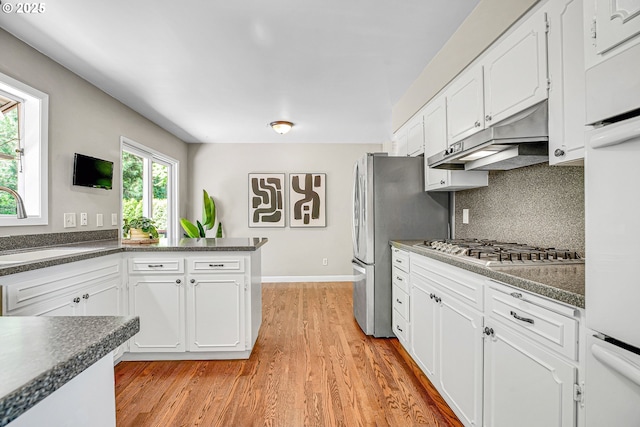 kitchen with under cabinet range hood, stainless steel appliances, dark countertops, and white cabinetry