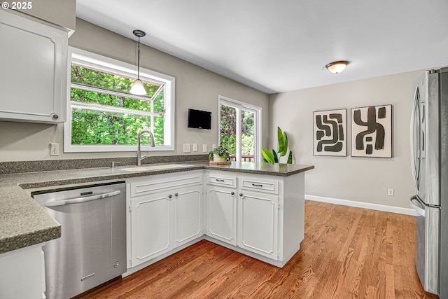 kitchen featuring appliances with stainless steel finishes, a sink, white cabinets, dark countertops, and wood finished floors