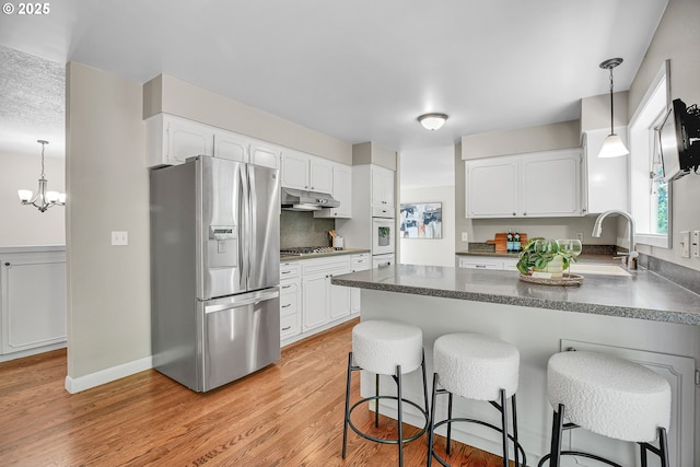 kitchen featuring appliances with stainless steel finishes, under cabinet range hood, a sink, a peninsula, and light wood-type flooring