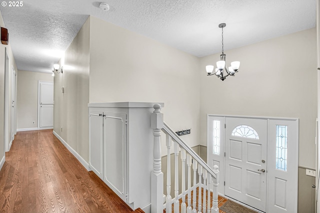 foyer entrance featuring a chandelier, a textured ceiling, wood finished floors, and baseboards