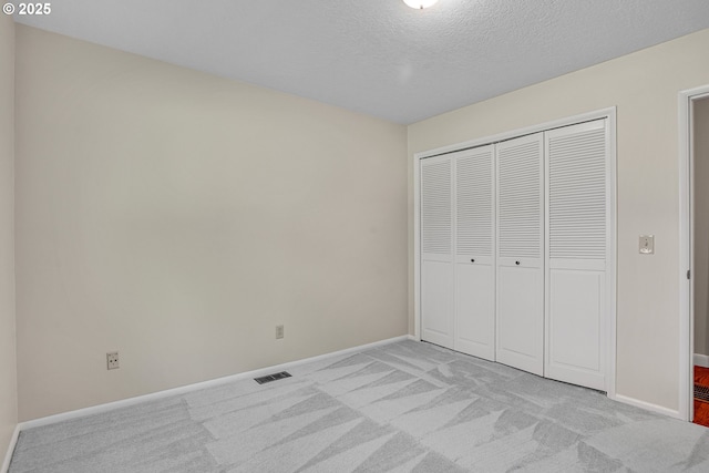 unfurnished bedroom with light colored carpet, baseboards, a closet, and a textured ceiling