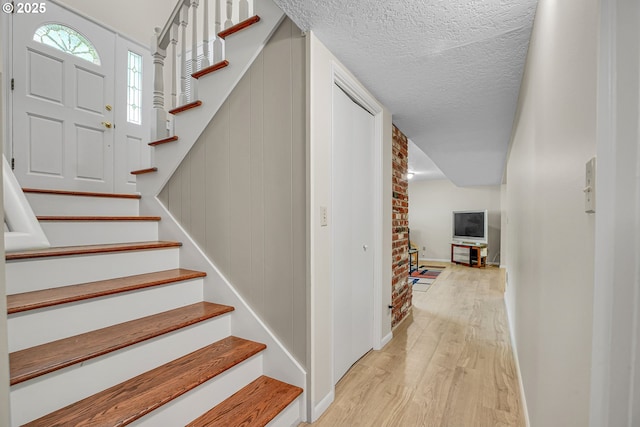 stairway with wood finished floors, baseboards, and a textured ceiling