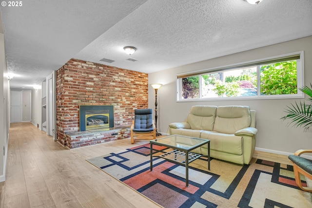 living room with a textured ceiling, wood finished floors, a brick fireplace, and baseboards