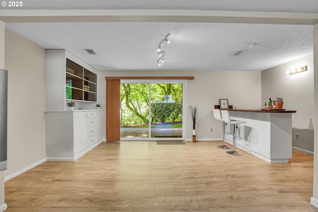 unfurnished dining area featuring light wood-style flooring, baseboards, a textured ceiling, and rail lighting