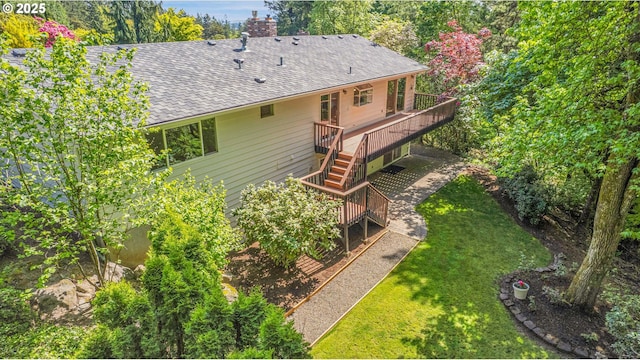 back of property featuring a deck, stairs, a shingled roof, a yard, and a chimney