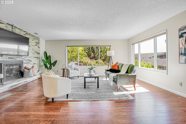 living area featuring wood finished floors, healthy amount of natural light, a textured ceiling, and a fireplace