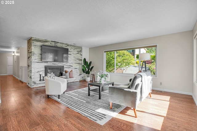 living area featuring wood finished floors, a fireplace, baseboards, and a textured ceiling