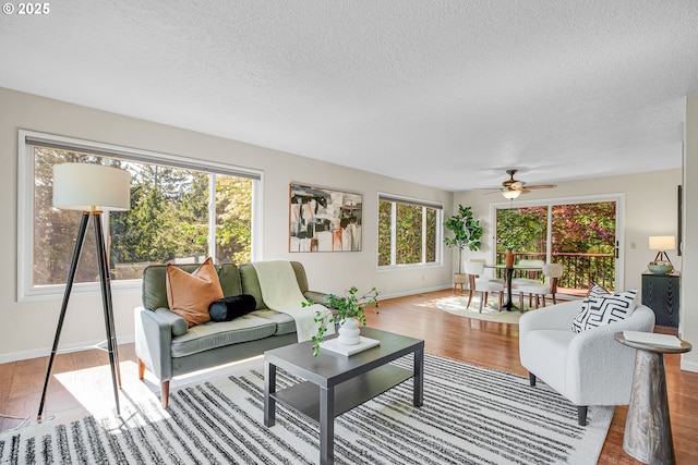 living area with wood finished floors, ceiling fan, a textured ceiling, and baseboards