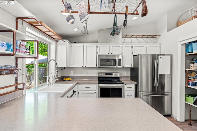 kitchen featuring stainless steel appliances, a sink, lofted ceiling, white cabinets, and light countertops