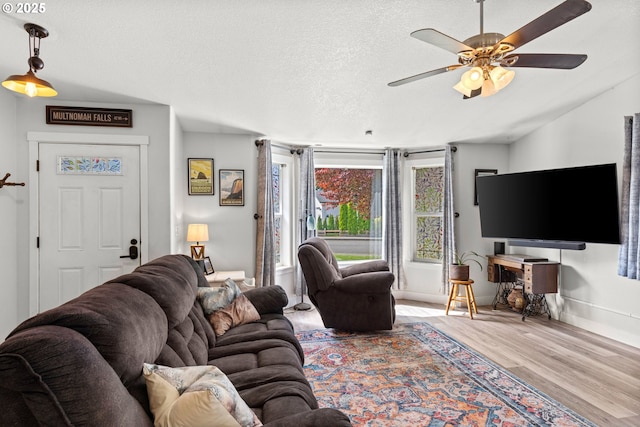 living room with wood finished floors, ceiling fan, baseboards, and a textured ceiling