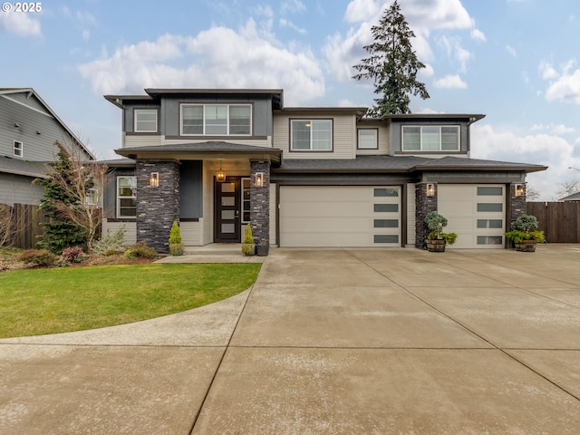 prairie-style home with a front lawn, fence, concrete driveway, stone siding, and an attached garage