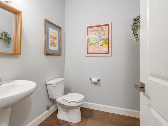 half bath featuring toilet, wood finished floors, baseboards, and a sink