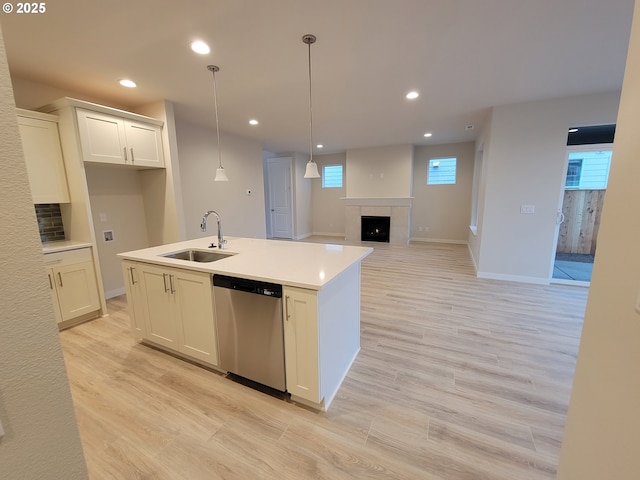 kitchen with dishwasher, white cabinetry, sink, a tiled fireplace, and a center island with sink