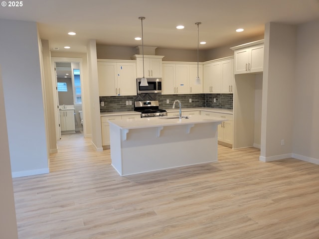 kitchen with hanging light fixtures, appliances with stainless steel finishes, a center island with sink, and light wood-type flooring