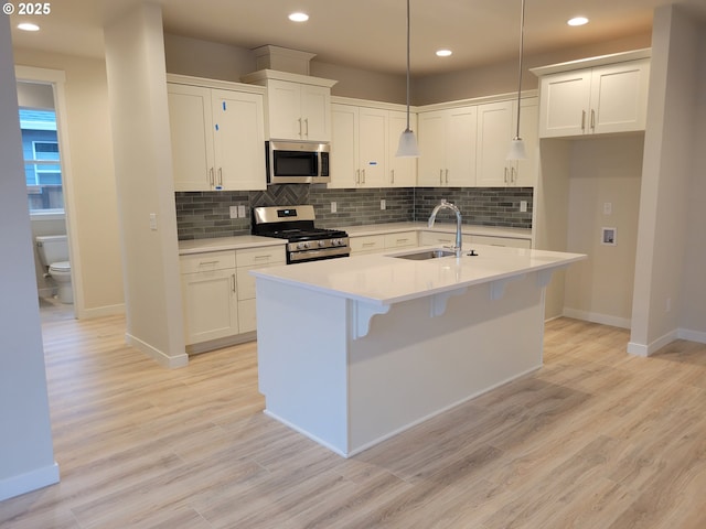 kitchen featuring decorative light fixtures, appliances with stainless steel finishes, light wood-style floors, white cabinetry, and a sink