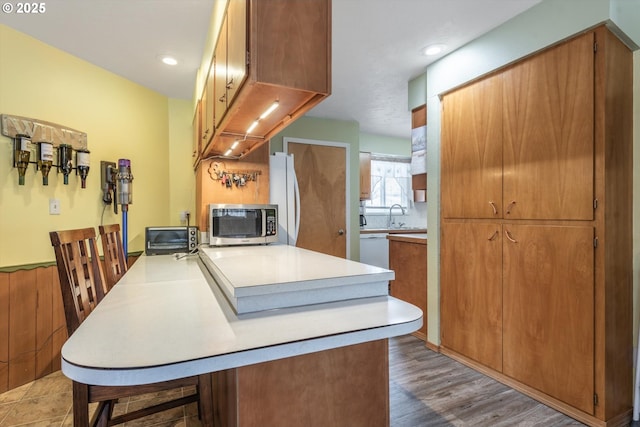 kitchen featuring a kitchen bar, a sink, white appliances, a peninsula, and light countertops