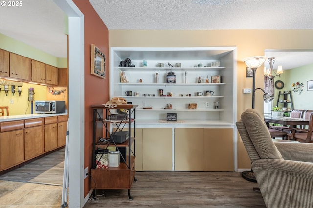 bar with stainless steel microwave, a textured ceiling, and wood finished floors