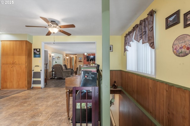 dining space featuring ceiling fan, wood walls, and wainscoting