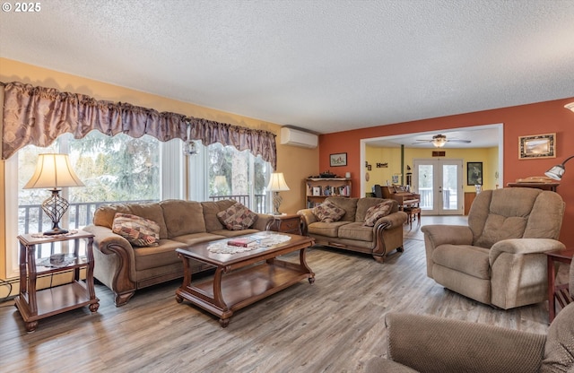 living room featuring a wall unit AC, light wood-style flooring, plenty of natural light, and french doors