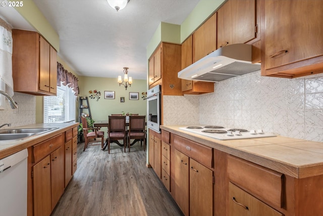 kitchen featuring white appliances, dark wood finished floors, a sink, under cabinet range hood, and a chandelier