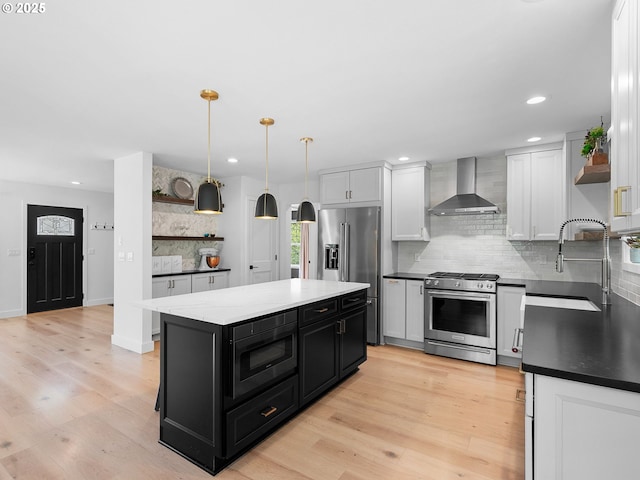 kitchen featuring open shelves, wall chimney exhaust hood, dark cabinetry, a sink, and stainless steel appliances