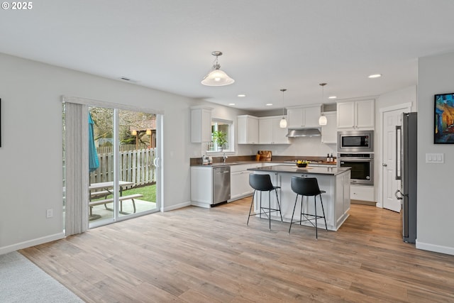 kitchen with a breakfast bar area, stainless steel appliances, a kitchen island, white cabinets, and decorative light fixtures