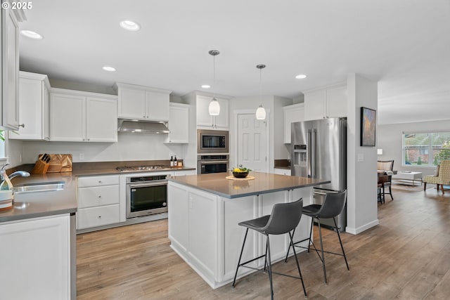 kitchen with stainless steel appliances, pendant lighting, a kitchen island, sink, and white cabinetry