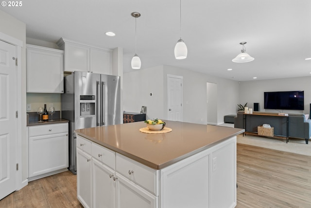 kitchen with light wood-type flooring, stainless steel fridge, a kitchen island, white cabinetry, and decorative light fixtures