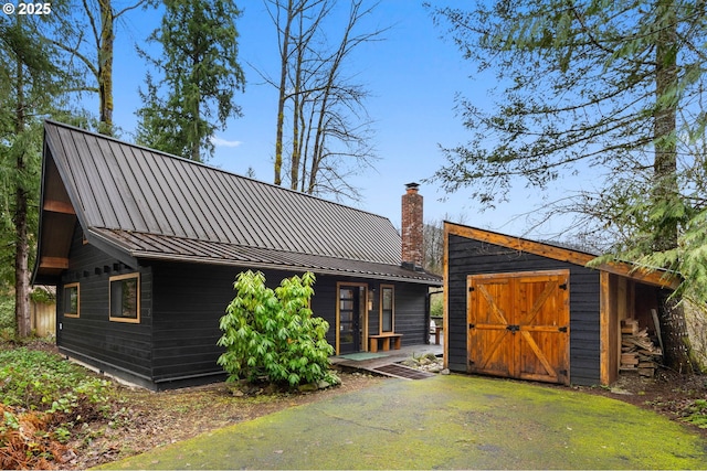 back of house with an outbuilding, a chimney, a standing seam roof, and metal roof