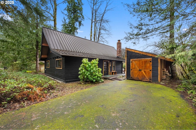 exterior space featuring a chimney, metal roof, an outbuilding, a storage unit, and a standing seam roof