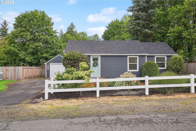 single story home featuring asphalt driveway, a shingled roof, a detached garage, and an outbuilding