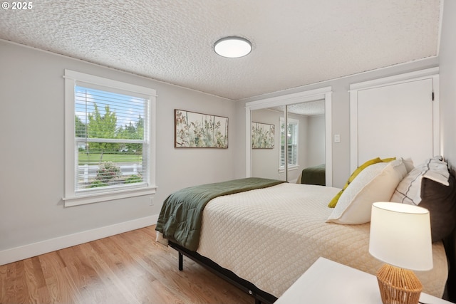 bedroom with light wood finished floors, a textured ceiling, baseboards, multiple windows, and a closet